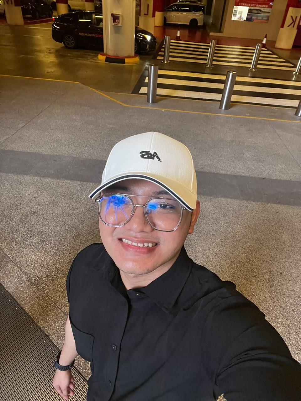 Mizan Adlani smiling, wearing a white cap, glasses and a black shirt